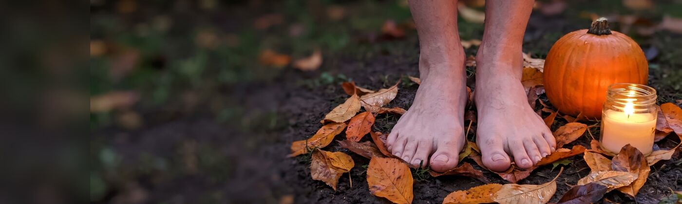 Pies descalzos sobre la tierra y hojas de otoño, junto a una calabaza y una vela al atardecer